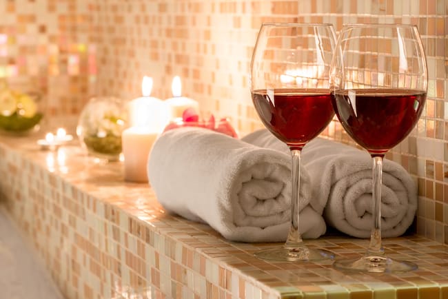 lit candles, towels and two glasses of wine on the bathroom ledge